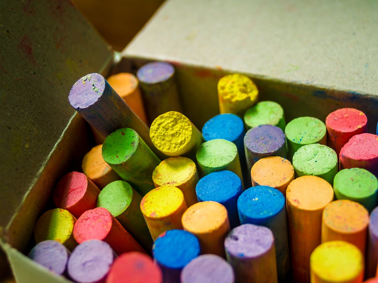 hero-homepage Close-up of colorful chalk sticks in an open box, showcasing a spectrum of vibrant hues.
