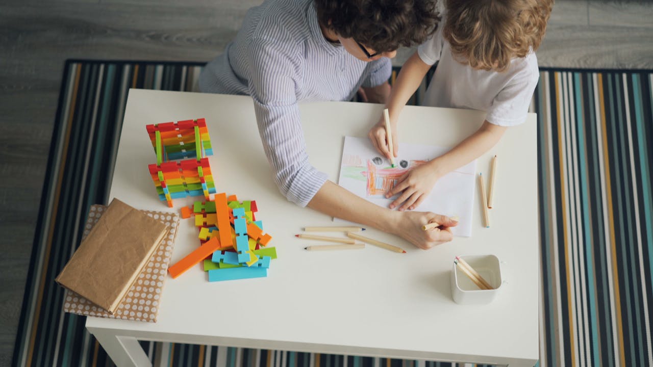 services-04 A mother and child engage in creativity with colored pencils at a table.